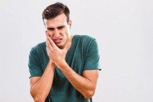 Man hold side of face in pain from a toothache and needing to see an emergency dentist in Falls Church VA.